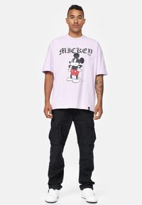 Fialové oversized tričko s grafikou Mickey Mouse v červených šortkách. V kombinaci s černými cargo kalhotami a bílými teniskami.