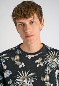 Musta lyhythihainen paita, jossa on valkoista, pinkkiä ja vihreää kukkakuviota. Omistaa pyöreän kaula-aukon, jossa on erottuva musta reunus.