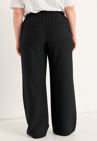 Svarta vida byxor med elastisk midja, med två bakfickor och en mjuk textur. Tyget verkar lätt och faller elegant.