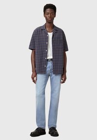Camicia a maniche corte a quadri in blu scuro e viola, abbinata a jeans azzurri e scarpe nere, presenta una vestibilità comoda e un design con bottoni.