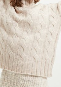 Pull en laine beige doux à torsades, avec un col montant, un ourlet raccourci, et un motif texturé avec des détails côtelés.