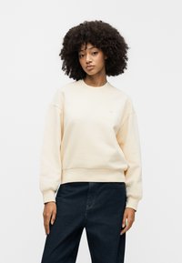 Ανοιχτό μπεζ φούτερ με στρογγυλή λαιμόκοψη, ριμπ μανσέτες και τελείωμα. Απαλή υφή, χαλαρή εφαρμογή και μικρή λογότυπο λεπτομέρεια στο στήθος.