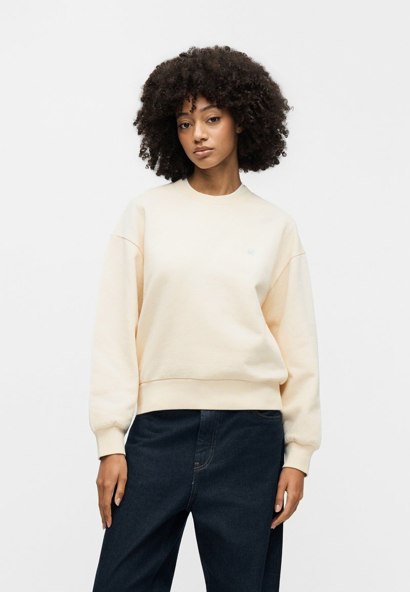 Hellbeiges Sweatshirt mit rundem Ausschnitt, gerippten Bündchen und Saum. Weiche Textur, lockere Passform und kleines Logodetail auf der Brust.