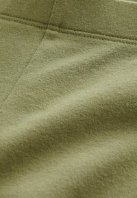 Tessuto verde oliva con una consistenza morbida, caratterizzato da motivi di tessitura visibili e un riflesso sottile. Presenta cuciture lungo i bordi.