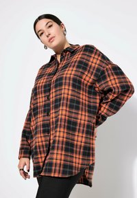 Camicia in flanella a quadri nera e arancione con bottoni anteriori, maniche lunghe e fessure laterali. Realizzata in un morbido tessuto testurizzato.