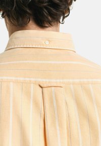 Hellorange gestreiftes Hemd mit Button-Down-Kragen, Rückenfalte und feiner Textur. Enthält einen einzelnen Knopf am Kragen.