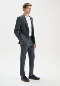 Costum gri cu o croială ajustată, închidere cu un singur nasture și buzunare laterale. Asortat cu un tricou alb și teneși navy. Textură de țesătură netedă.