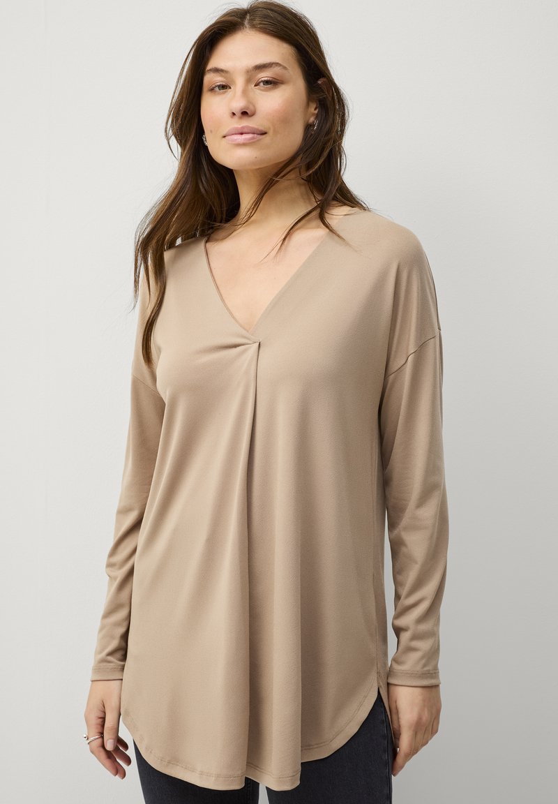 Beige langærmet top med V-hals og draperet design, der har en subtil plissering foran og en rundt afslutning. Glat stofstruktur.