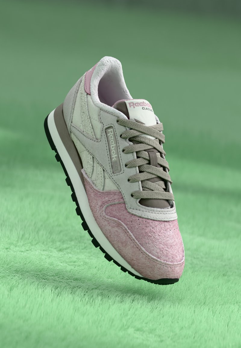 Sapatilhas com um cabedal em camurça cinza claro e rosa, detalhes em tecido e sola de borracha. Apresenta painéis texturizados e atacadores. Logótipo da Reebok presente.