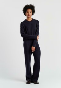 Pull en maille marine avec un col en V et des poignets côtelés, associé à un pantalon ajusté assorti. Texture douce et silhouette décontractée.