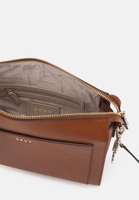 Brun texturerad läderhandväska med en guldfärgad dragkedja, innerfack och DKNY-märke. Har en slät foder och en strukturerad design.