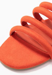 Sandalo in suede arancione con tre cinturini orizzontali sulla parte superiore, suola piatta e una fodera interna liscia.