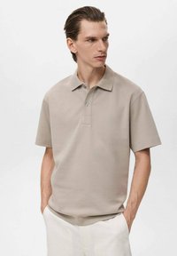 Beige polo skjorta tillverkad av slätt tyg, med klassisk krage, treknäppning och korta ärmar. Enkel, minimalistisk design.
