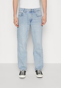 Light blue denim jeans with a relaxed fit, featuring five pockets, a button closure, and subtle fading on the fabric. Paired with black sneakers.
