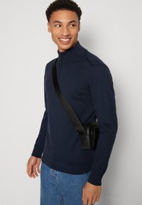 Suéter azul marino con cuello alto, tejido texturizado, combinado con jeans azul claro y un pequeño bolso cruzado negro.