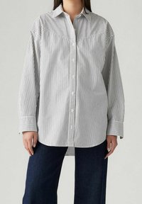 Chemise à rayures boutonnée en noir et blanc, dotée d'un col classique, d'une poche poitrine et de larges poignets. Tissu doux avec une coupe décontractée.