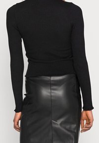 Černý žebrovaný pletený svetr s dlouhými rukávy, kombinovaný s černou koženou sukní s vysokým pasem a hladkým, lesklým povrchem.