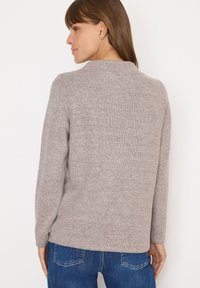 Pull en tricot gris avec une texture douce, col rond et manches longues. Présente des fentes sur les côtés au niveau de l'ourlet pour faciliter le mouvement.