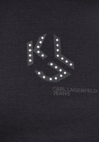 Juodas medvilninis marškinėlis su grafikiniu logotipu, papuoštu baltais kalnų kristalais, centre rašant "Karl Lagerfeld Jeans". Švelni tekstūra.