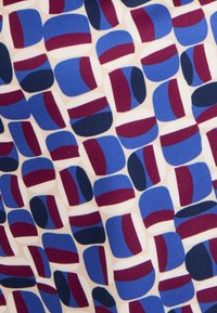 Tessuto geometrico con forme astratte in tonalità di blu, borgogna e crema, caratterizzato da una texture liscia e un motivo colorato e ripetitivo.