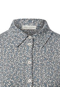 Blue floral blouse with a collar. Small white flowers on a textured pattern, featuring white buttons and a brand label inside the collar.