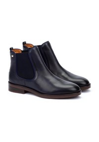 Bottines Chelsea en cuir bleu marine avec panneaux latéraux élastiques et bouts ronds. Les semelles texturées marron et la finition lisse donnent une apparence élégante.