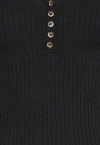 Tissu côtelé noir avec une rangée verticale de six boutons marron, chacun avec quatre trous, centrée le long de la patte de tissu.