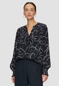 Blouse noire à motifs de cœurs blancs, avec un bouton à l'avant, manches longues à poignets froncés et coupe décontractée. Tissu léger.