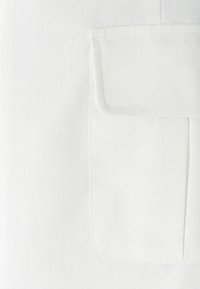 Biela tkanina s textúrovanou väzbou, s náprsnou kapsou na ľavej strane a záhybom pod kapsou.