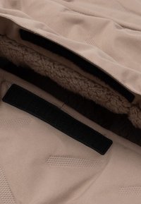 Beige buitenstof met zachte, gestructureerde voering. Bevat zwarte klittenbandsluiting en subtiele reliëfpatronen. Beschikt over een veilige, gesloten ontwerp.