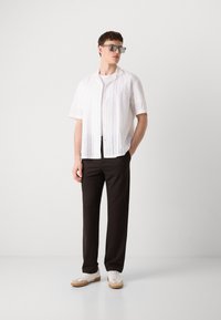 Witte korte mouwen overhemd met textuurpatroon, gecombineerd met zwarte broek en witte sneakers met beige accenten.