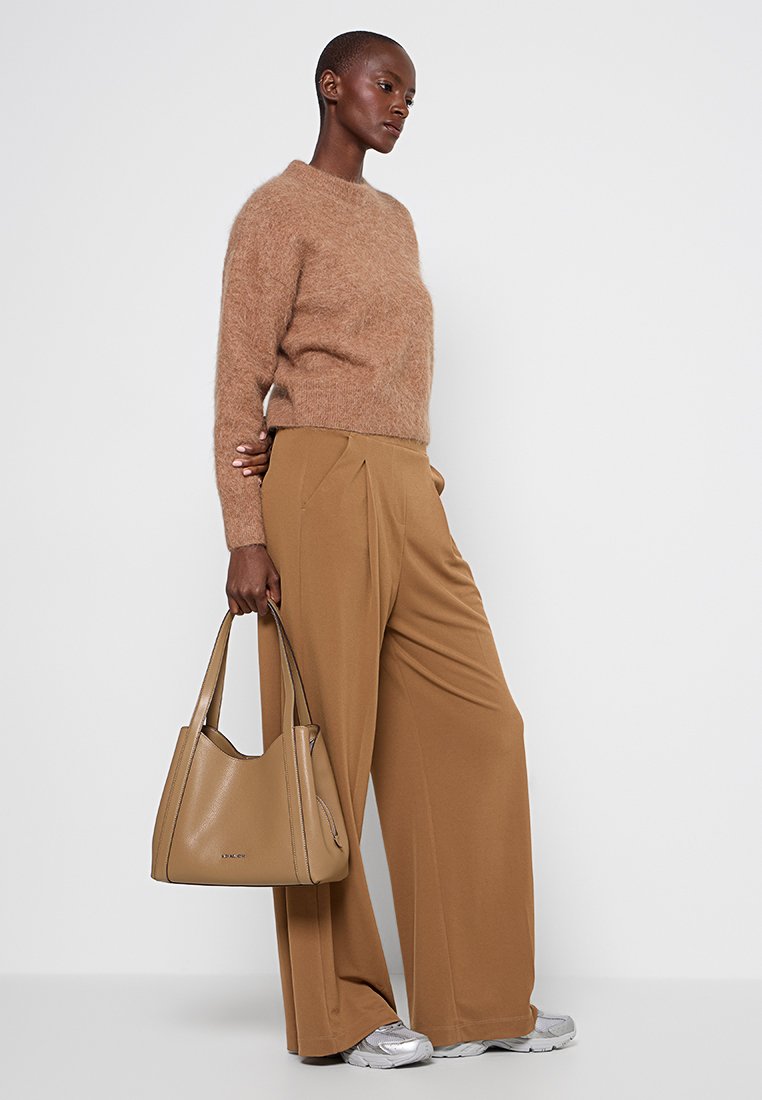 Brun fluffig tröja, tan färgade vida byxor, silverfärgade sneakers och en beige handväska med en rundad design som visar en slät yta.