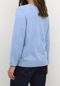 Light blue knitted sweater with a round neckline, long sleeves, and ribbed hem, paired with dark denim jeans featuring patterned stitching.