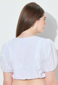 Top bianco accorciato con maniche a sbuffo, texture a coste e scollatura rotonda. Tessuto morbido con una finitura pulita all'orlo.
