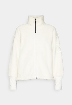 Balta, pūkuota zip-up striukė su aukštu kaklu, numestais pečiais ir raukšlėtomis rankovėmis. Pasižymi kontrastinga juoda užtrauktuku ir subtilia tekstūra.