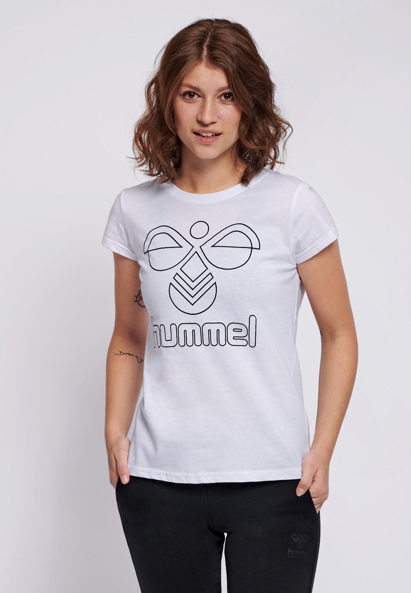 Weißes Kurzarm-T-Shirt aus Baumwolle mit einem schwarzen Grafiklogo und dem Text "hummel" auf der Vorderseite. Kombiniert mit schwarzen Hosen.