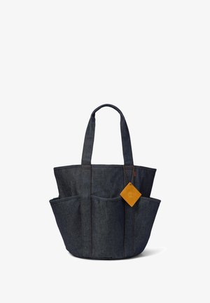 Torba na ramię z ciemnego denimu z dwoma uchwytami, trzema zewnętrznymi kieszeniami i małą brązową skórzaną metką przymocowaną do jednego uchwytu.