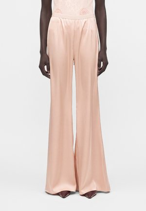 Γυναίκα με ψηλόμεσο, φαρδύ ρόζ σατέν παντελόνι συνδυασμένο με μπορντό μυτερά παπούτσια, εμφανίζεται από τη μέση και κάτω.