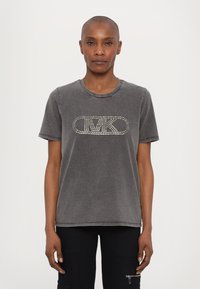 Camiseta de algodón gris con cuello redondo, mangas cortas y un diseño de logo con clavos plateados en el frente. Textura ligeramente desgastada.