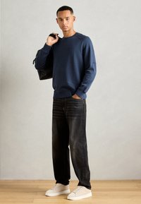 Marineblå sweatshirt med raglanermer, kombinert med mørke denimjeans. Hvite sneakers og en svart veske fullfører antrekket. Enkelt og moderne design.