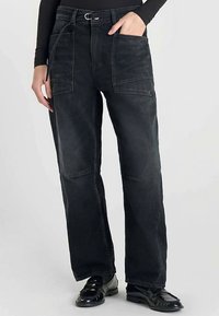 Pantalon en denim noir à coupe ample, avec deux grandes poches frontales, une taille ceinturée et un léger effet délavé sur l'ensemble du tissu.
