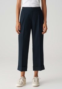 Pantalons ample bleu marine avec une taille élastique haute. Présente des ourlets à revers et un tissu lisse et texturé. Portés avec des baskets claires.