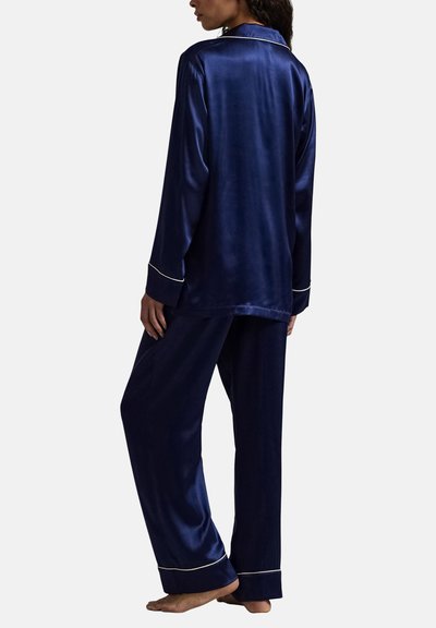 Marineblauw satijnen pyjamaset met lange mouwen, witte biesdetails, losse broek en een ontspannen silhouet. Zachte textuur met een gladde afwerking.