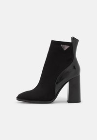 Bottines noires à bout pointu, alliant daim et cuir verni brillant. Talon solide et bloc avec un accent logo en forme de triangle.