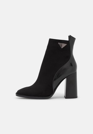 Black ankle boot featuring a pointed toe and a combination of suede and glossy patent leather. Solid block heel with a triangular logo accent.