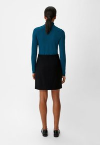 Haut à manches longues en teal associé à une jupe crayon noire, affiché de dos. La tenue présente un design épuré et une silhouette ajustée.