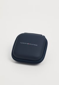 Kompaktna tamnoplava kvadratna torbica s patentnim zatvaračem, zaobljenih rubova, s logotipom Tommy Hilfiger smještenim u središtu gornje površine.