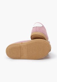 Papuci din suede roz, cu un accent alb pe spate. Prezintă o talpă texturată din cauciuc, cu striații. Arată un material moale și o formă rotunjită.