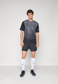 Nike sportoutfit met een verloop van grijs naar zwart korte mouwen shirt, zwarte shorts, witte knie-lange sokken en zwarte sport schoenen.