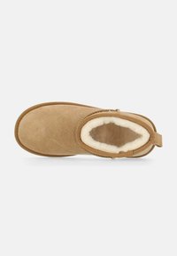 Stivale alla caviglia in suede marrone con una morbida fodera in pelliccia color crema, punta rotonda, suola piatta e una linguetta posteriore per una facile calzata.